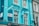 A bright blue building with large windows is decorated with a string of hanging lights. A street sign reads 'Kingly Street W1, City of Westminster' against the vibrant background. The architecture features classic elements, and there are floral decorations visible.