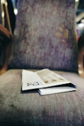 A folded magazine or brochure lies on a patterned fabric chair with a blurred background indicating an indoor setting.