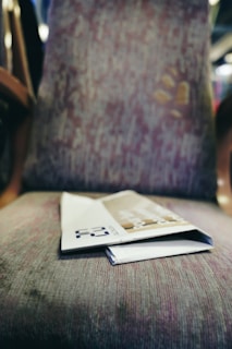 A folded magazine or brochure lies on a patterned fabric chair with a blurred background indicating an indoor setting.