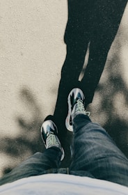 A model walking down a city street wearing dark blue jeans and crisp white sneakers, sunlight casting soft shadows.