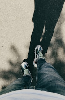 A model walking down a city street wearing dark blue jeans and crisp white sneakers, sunlight casting soft shadows.