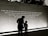 A large wall displays an inspirational quote, with two individuals silhouetted against it. The quote calls for peace and broader perspectives beyond societal divisions. The scene is captured in low light or a sepia tone, creating a contemplative atmosphere.