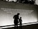 A large wall displays an inspirational quote, with two individuals silhouetted against it. The quote calls for peace and broader perspectives beyond societal divisions. The scene is captured in low light or a sepia tone, creating a contemplative atmosphere.
