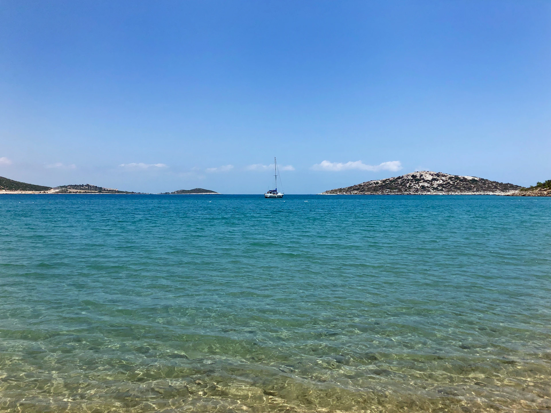 A crystal-clear turquoise ocean with a lone sailboat drifting near a tropical island.