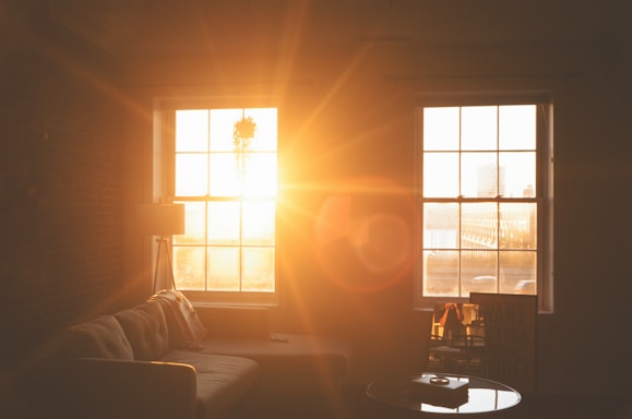 A clean, bright living room with sunlight streaming through large windows.