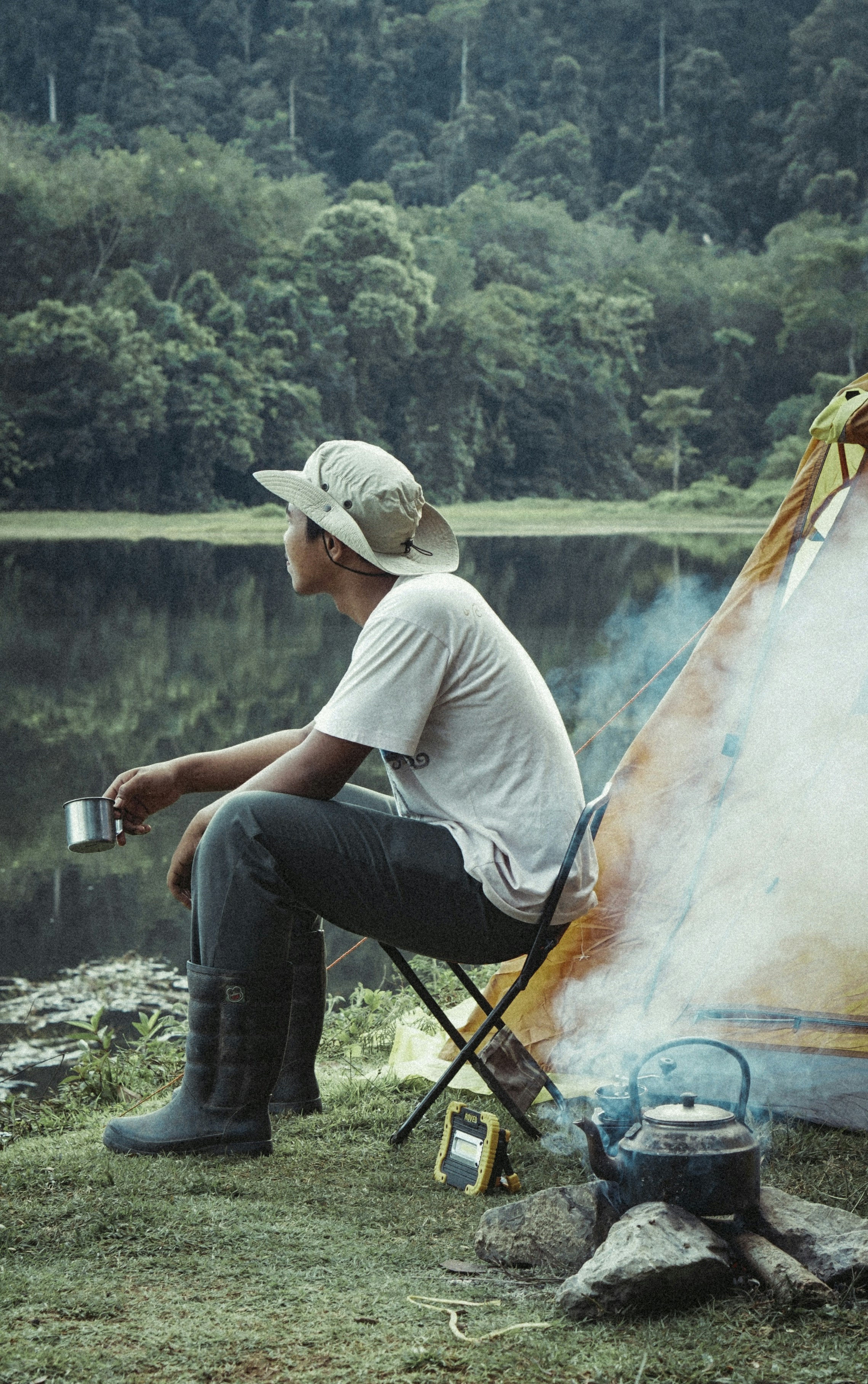 A person sitting a campsite beside a river. 