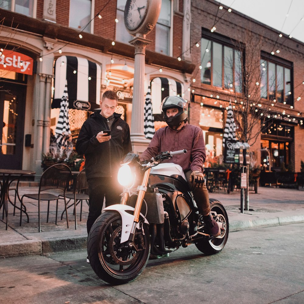 man standing using smartphone beside man riding motorcycle