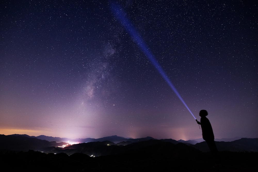 man standing on peak while holding flash light at night