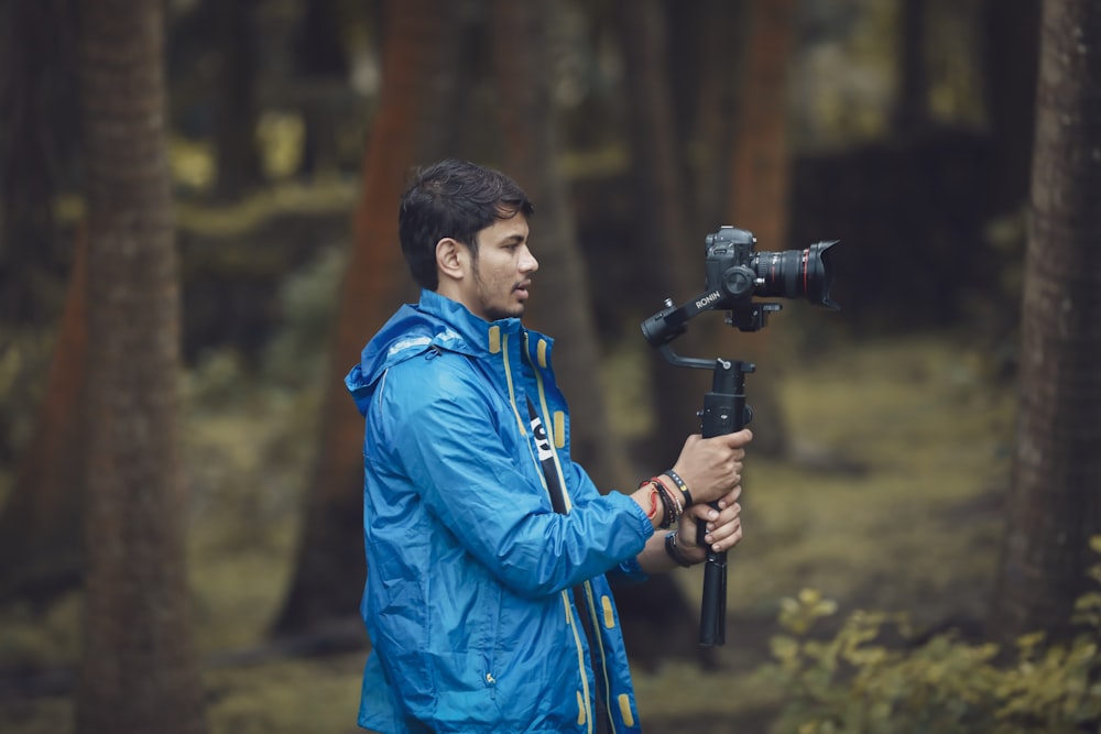 man wearing blue jacket holding tripod with DSLR