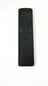 A black remote control with several buttons, including a circular directional pad, power button at the top, and volume control. The surface appears matte with a minimalist design.