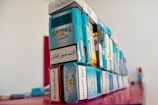 A stack of various cigarette packs, prominently featuring the Camel brand, arranged on a red surface. The packs display warning labels in different languages. The image has a shallow depth of field, with the focus on the nearer packs and a blurred background.
