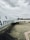An airplane branded with 'American Eagle' is parked on the tarmac under a cloudy sky. The aircraft is positioned diagonally in the frame with its tail visible. A worker in a high-visibility vest and some luggage carts are nearby.