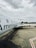 An airplane branded with 'American Eagle' is parked on the tarmac under a cloudy sky. The aircraft is positioned diagonally in the frame with its tail visible. A worker in a high-visibility vest and some luggage carts are nearby.