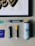 A collection of art supplies is displayed on a light gray surface. The items include a framed artwork featuring stylized text in black and gold, several markers, a spray paint can, and a small purple booklet. The markers are of different sizes, with one having a yellow cap. A small sticker with colorful text is also visible.