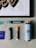 A collection of art supplies is displayed on a light gray surface. The items include a framed artwork featuring stylized text in black and gold, several markers, a spray paint can, and a small purple booklet. The markers are of different sizes, with one having a yellow cap. A small sticker with colorful text is also visible.