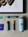 A collection of art supplies is displayed on a light gray surface. The items include a framed artwork featuring stylized text in black and gold, several markers, a spray paint can, and a small purple booklet. The markers are of different sizes, with one having a yellow cap. A small sticker with colorful text is also visible.