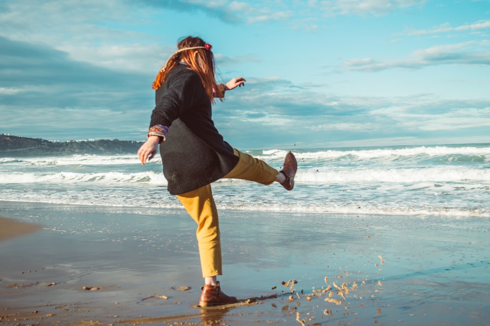 person in black top, yellow pants, and brown boots on shore