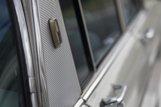 Close-up view of a section of a classic car's exterior, highlighting the shiny metal surface and textured details near the window area.