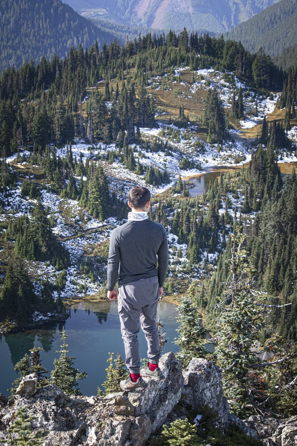 man wearing gray long-sleeved shirt standing on rock across green trees