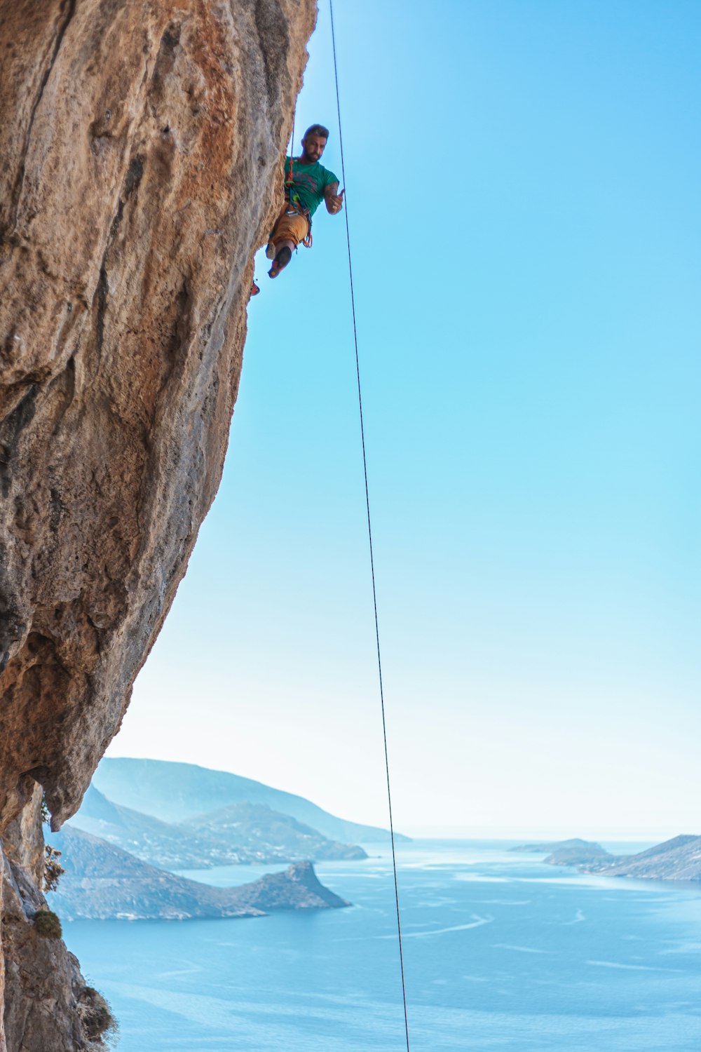 man climbing on brown mountain above body of water