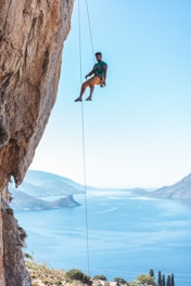 man hanging on rope on cliff during daytime
