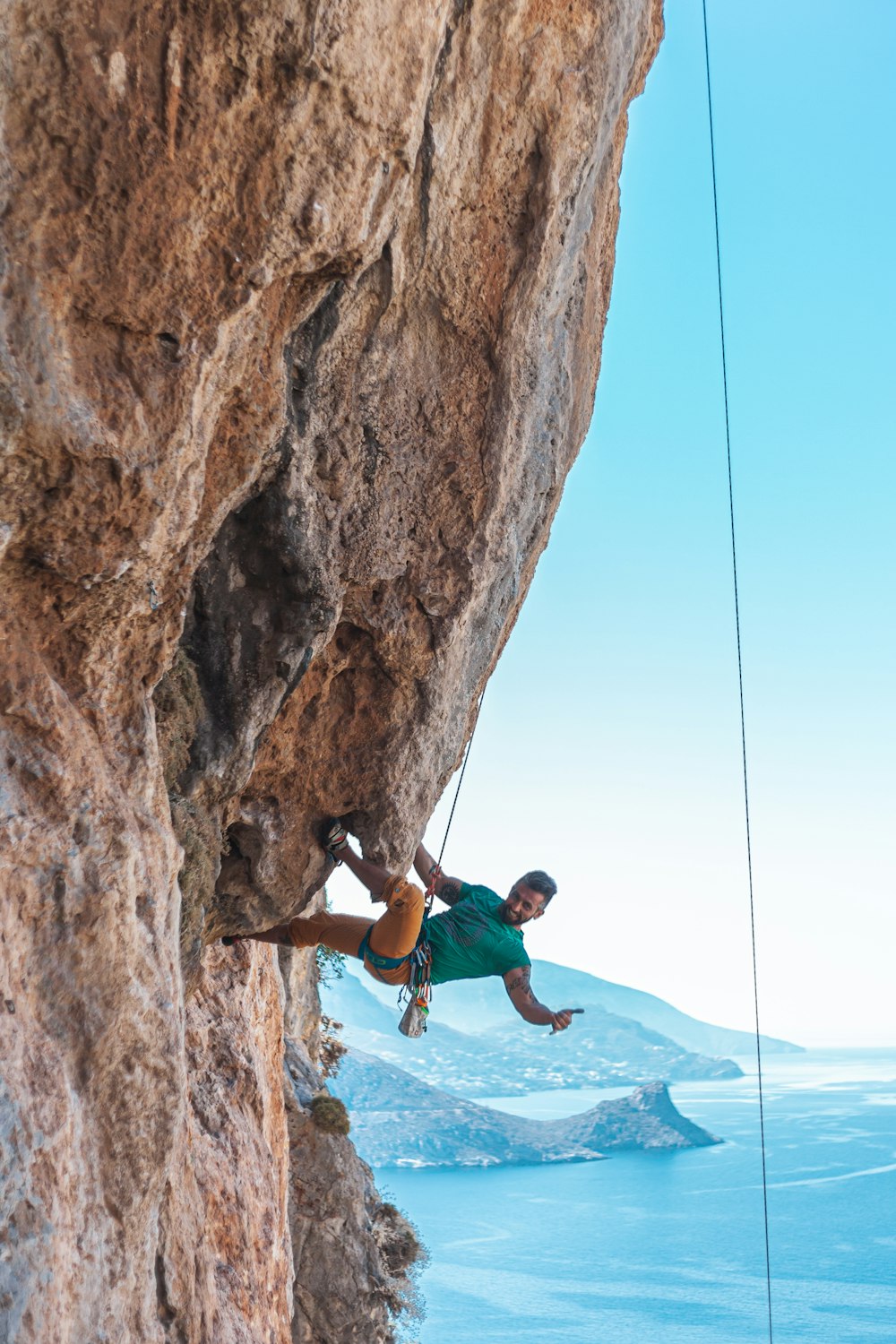 man in teal shirt climbing rock formation
