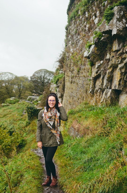 woman wearing gray jacket standing while touching her hair on green field in Rock of Cashel Ireland