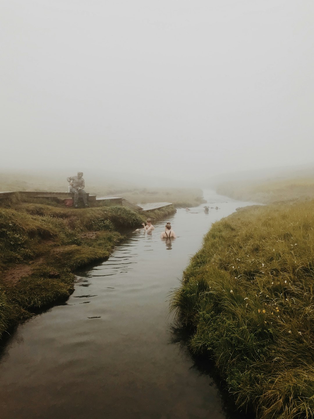 people in river near green field covered with fogs during daytime
