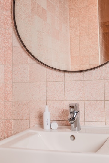 A clean bathroom sink area with a bottle of rahman llc stain remover placed beside a mirror.