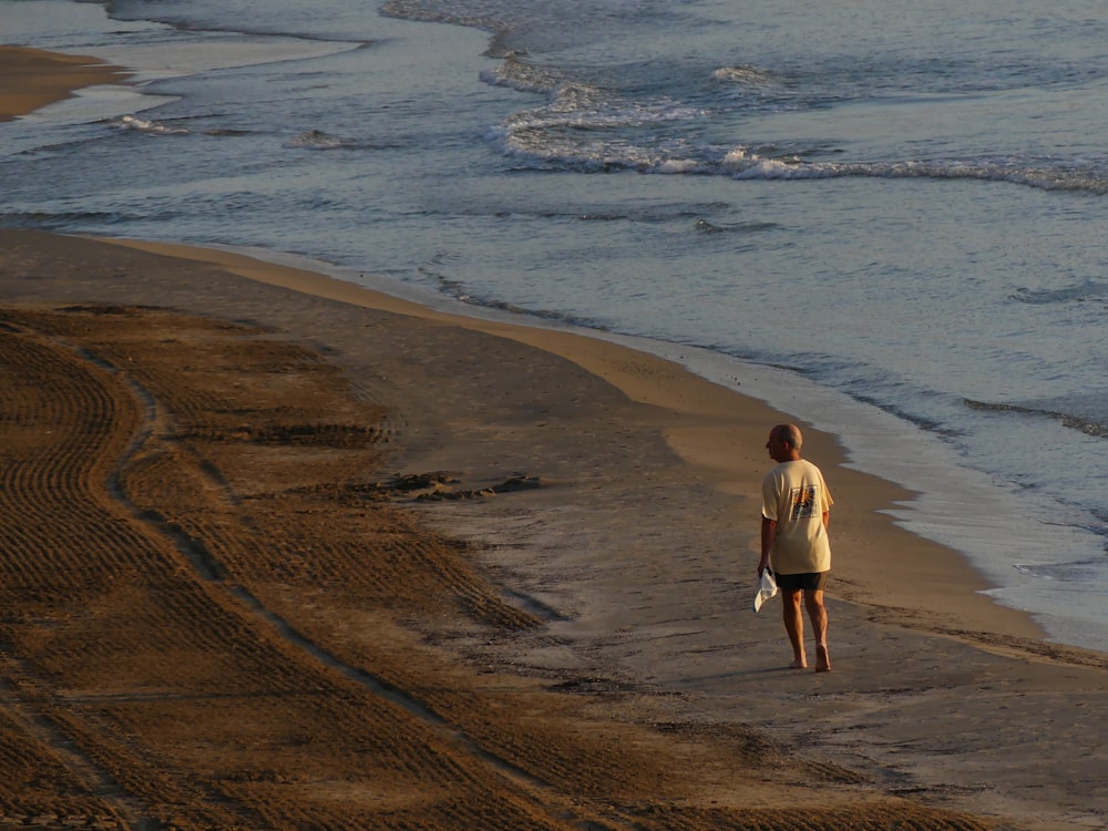 man wearing white shirt walking on seashore