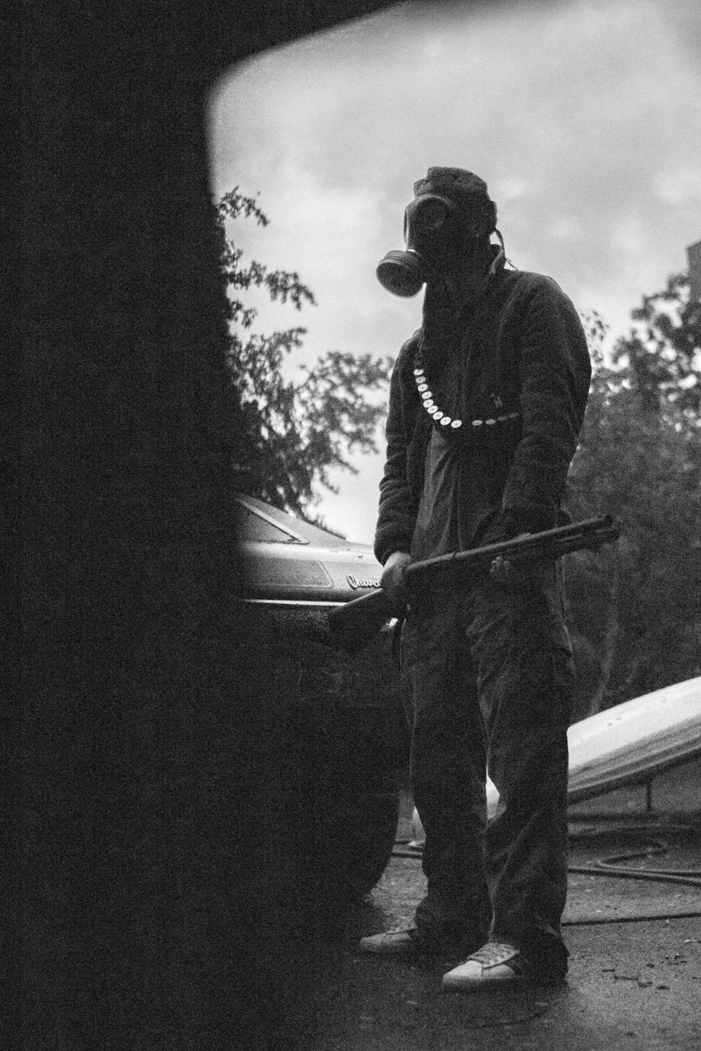 man with gas mask and holds rifle at the back of the car