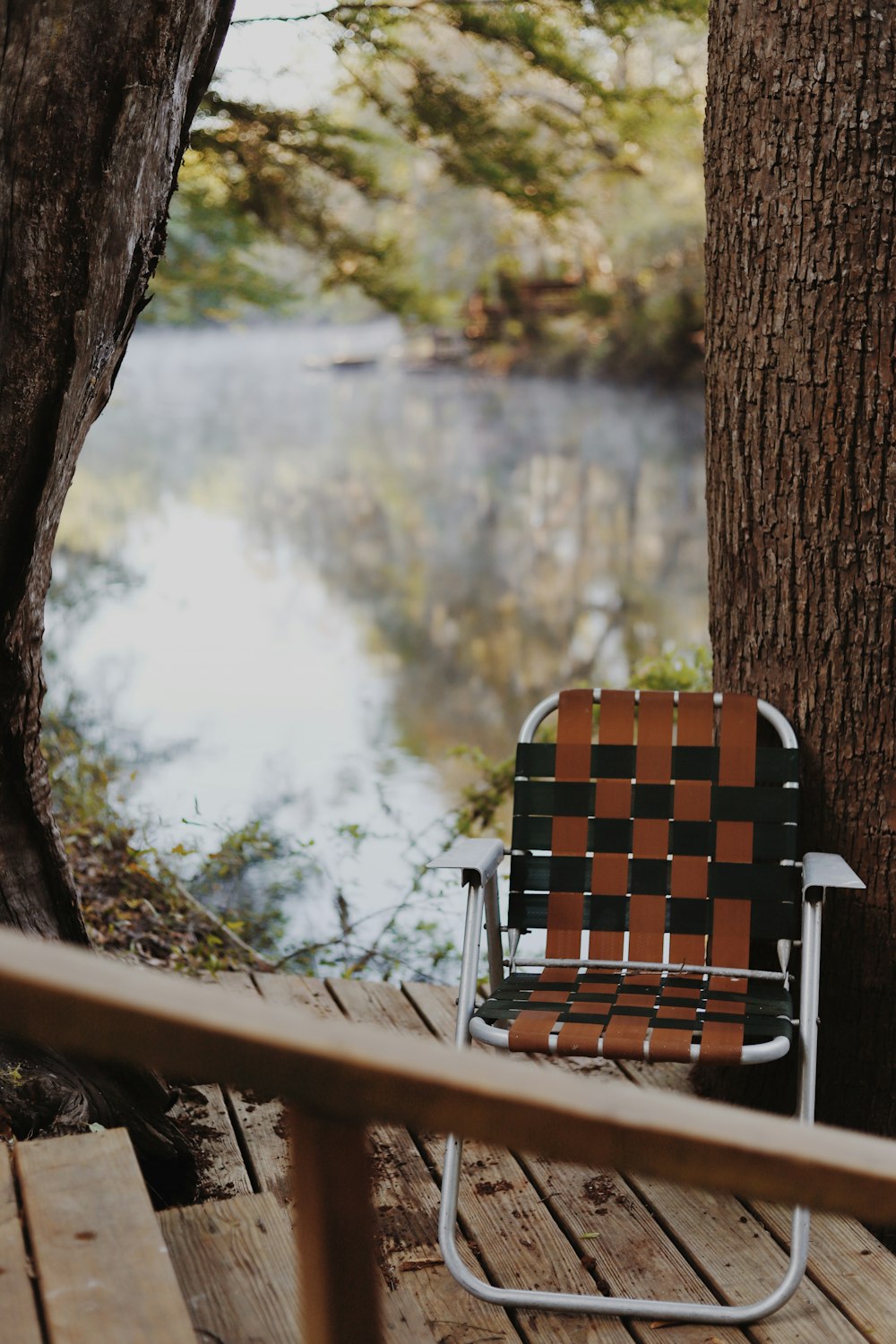 folding web chair beside tree near body of water