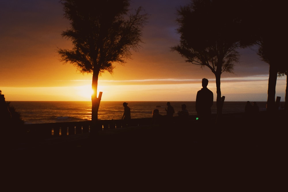 a group of people sitting on a bench watching the sun set