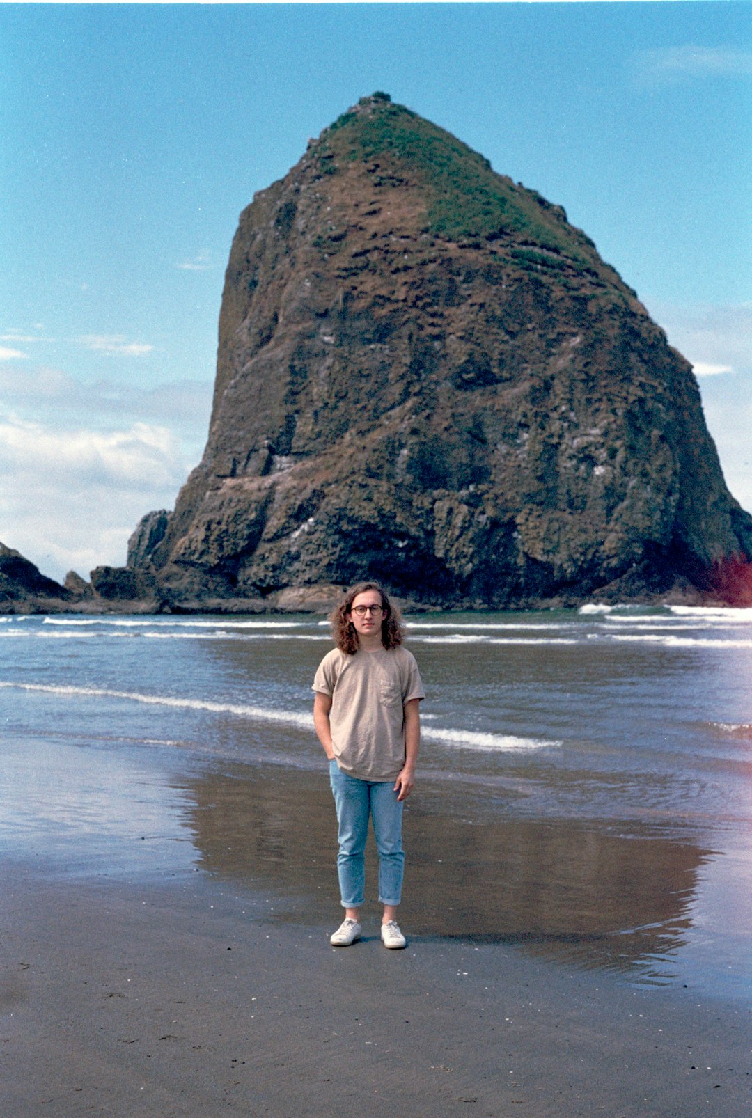 man standing on shore behind sea stack