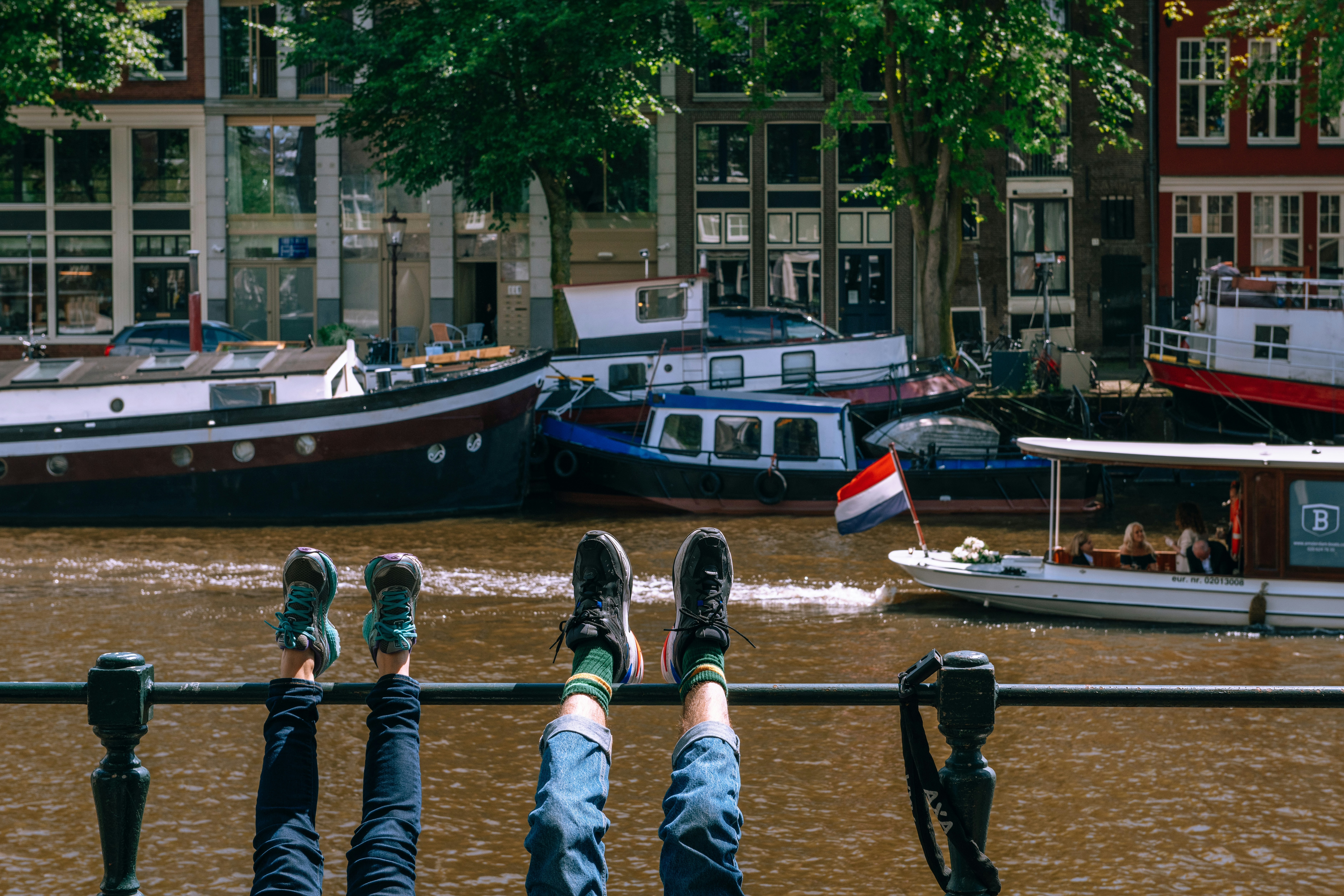 two person leaning feet on black metal fence beside river