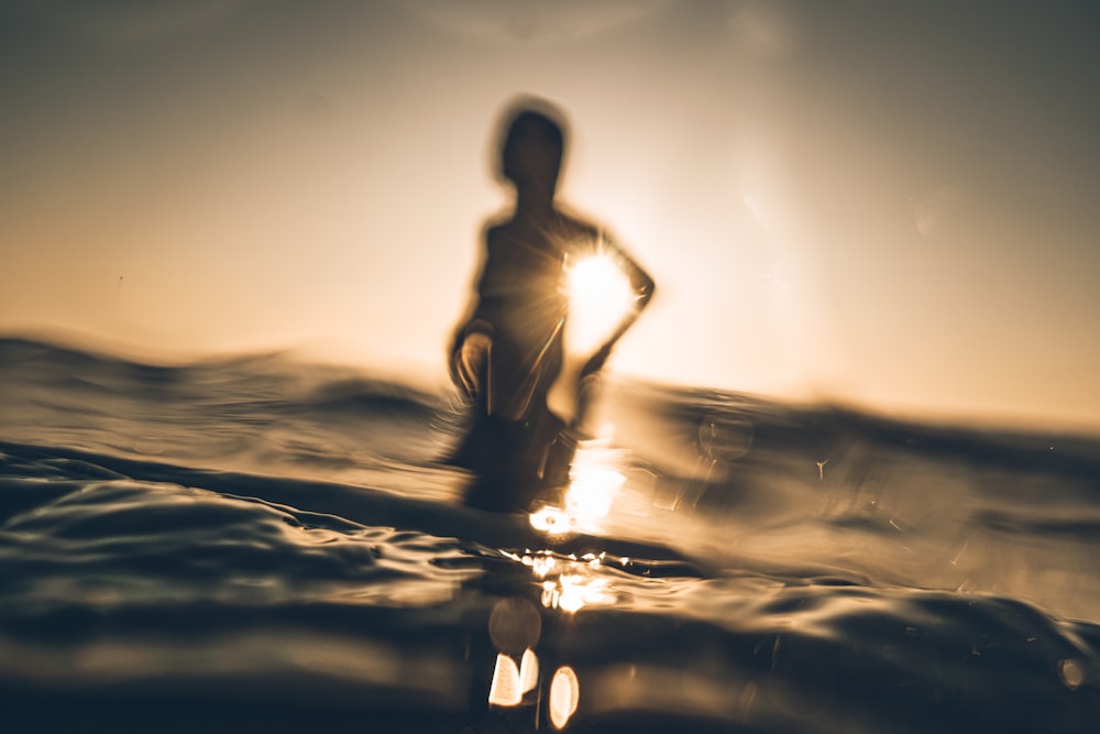silhouette of person standing on sea wave during daytime