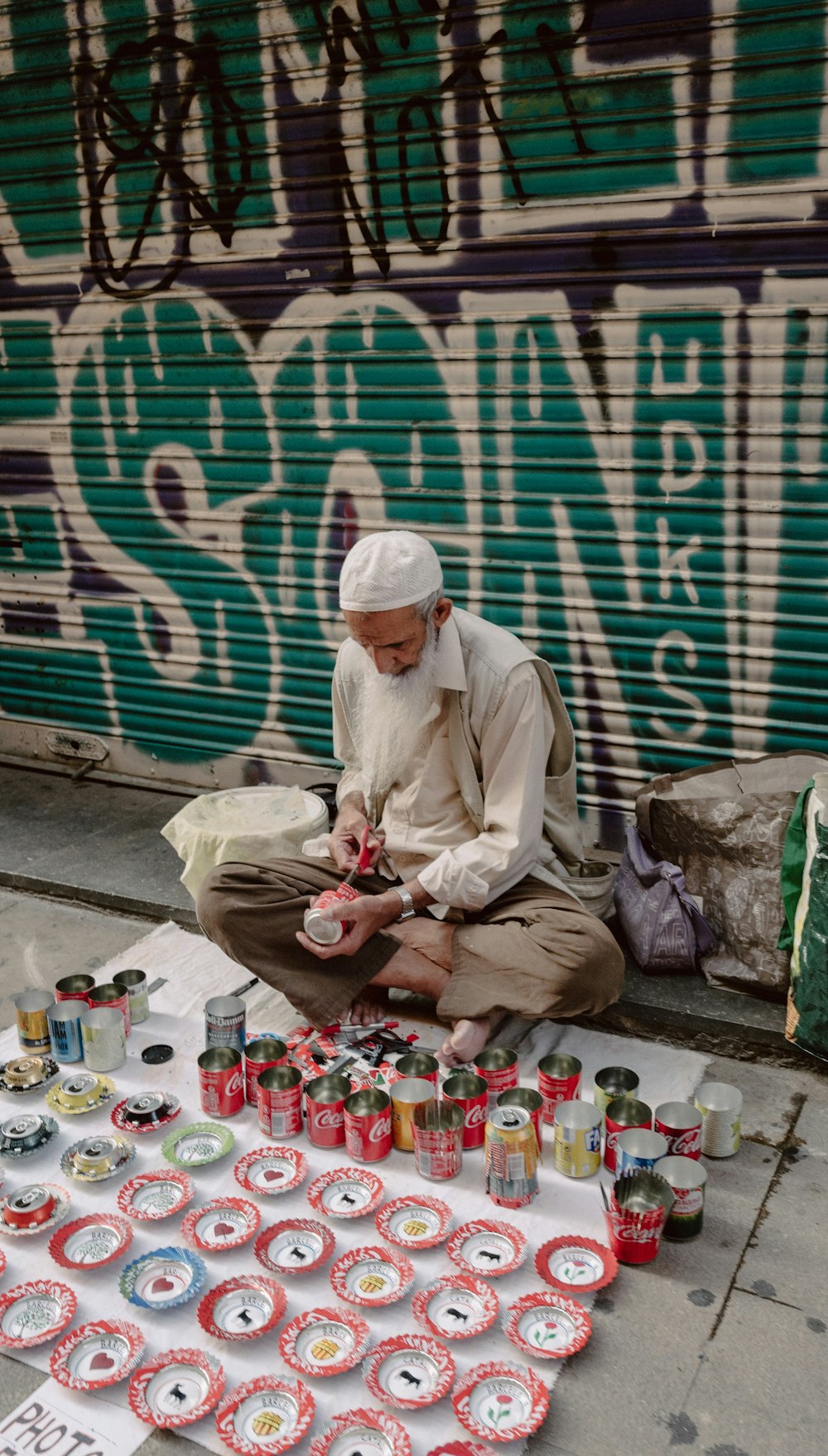 歩道に座って缶の装飾をしている男