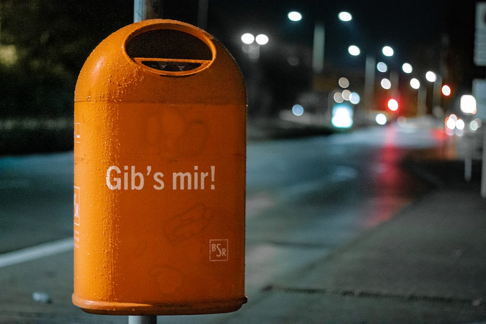 orange metal trash bin by roadside at nighttime