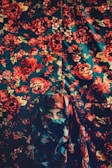A person wearing a colorful, patterned headscarf is partially veiled against a background that also features a vivid floral design. The colors blend harmoniously with the backdrop, creating a seamless and artistic integration.
