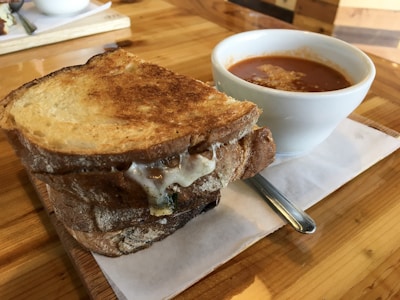 A grilled cheese sandwich with melty cheese and a cup filled with tomato soup