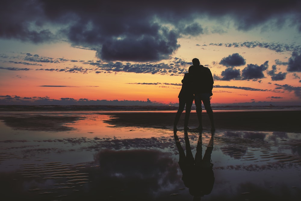 silhouette of two person standing near seashore