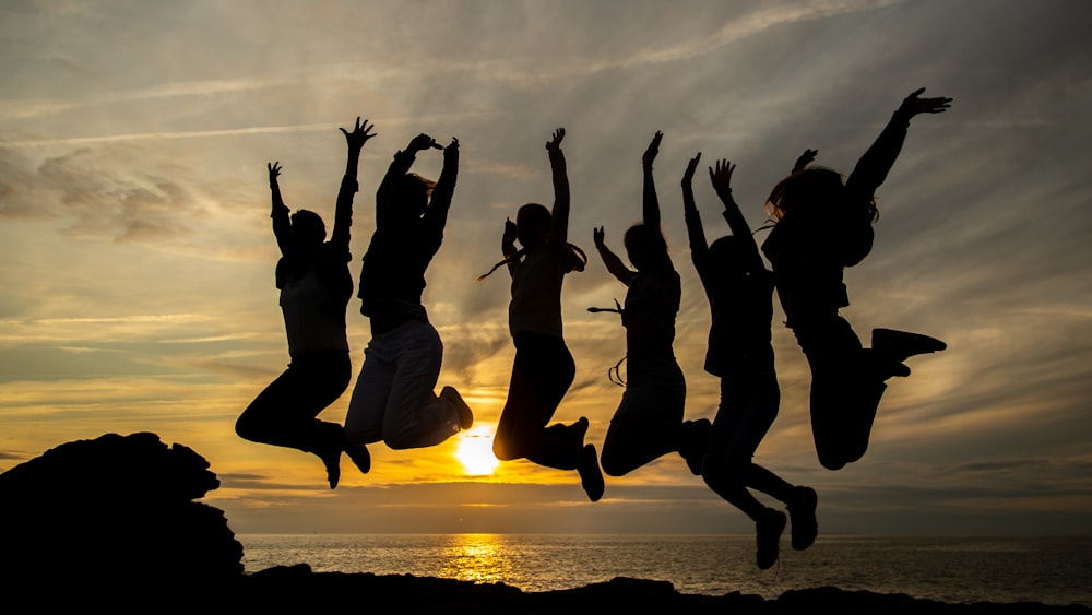silhouette of six women jumping beside seashore