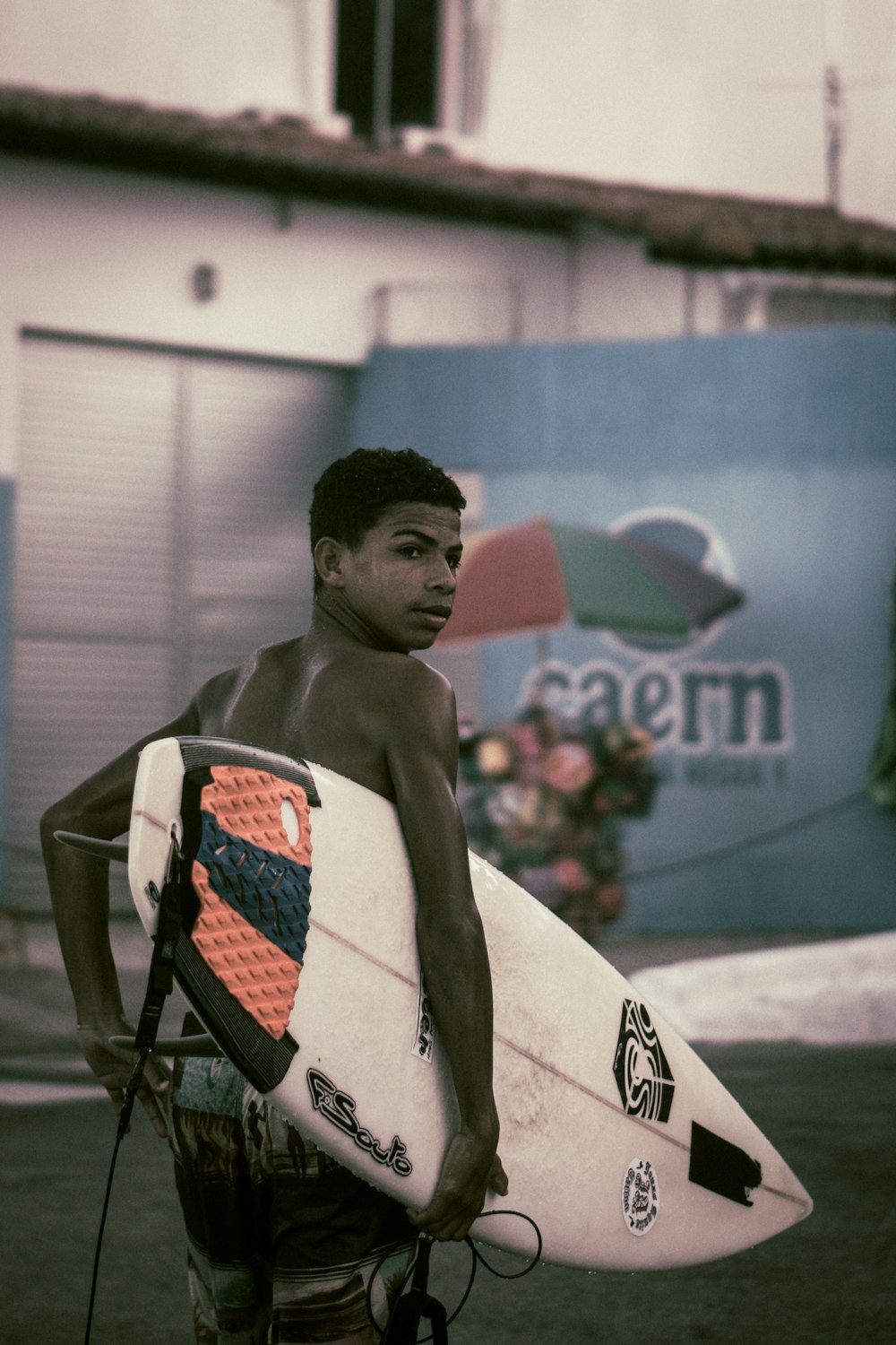 topless boy carrying surfboard