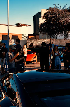 A diverse group of happy customers standing beside a Porsche Macan and a Range Rover Sport in a sunlit Arizona desert setting.