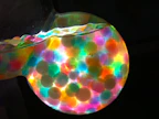 Brightly colored crunchy slime with beads and foam balls spilling out of a clear container