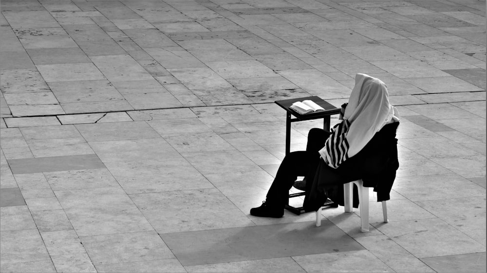 grayscale photo of person sitting on plastic chair