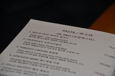 A menu card featuring various pasta dishes with names and descriptions written in both English and Korean. The section shown lists dishes such as Aglio-Olio, Crudaíola, Vongole Linguini, and Genovese with accompanying prices.
