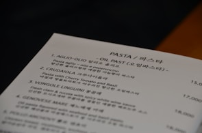 A menu card featuring various pasta dishes with names and descriptions written in both English and Korean. The section shown lists dishes such as Aglio-Olio, Crudaíola, Vongole Linguini, and Genovese with accompanying prices.
