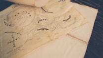A vintage-style map depicting fictional locations such as Rohan, Gondor, and Mordor, with an artistic design that includes topographical details and labels. The worn paper and sepia tones give it an aged appearance.