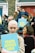 A group of people gathered outside with signs that read 'TRUTH JUSTICE LOVE' in bold yellow letters on a blue background. The crowd includes a diverse mix of individuals, some holding cameras, with expressions ranging from focused to contemplative. The background features red and blue doors with brick walls.